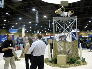 A vendor talks to attendees at the Border Security Expo in Phoenix, Ariz., next to a display of sophisticated cameras and sensors painted to blend into the desert. A vendor talks to attendees at the Border Security Expo in Phoenix, Ariz., next to a display of sophisticated cameras and sensors painted to blend into the desert.