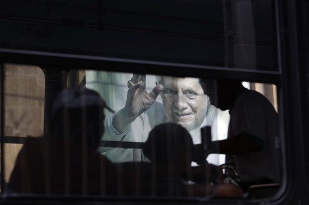 In this Feb. 29, 2012 photo, people riding on a bus pass a banner of Pope Benedict XVI on the wall of a church in Leon, Mexico.