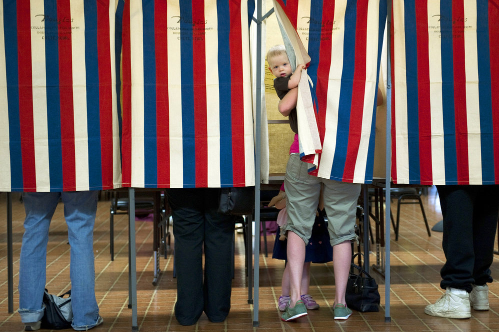Landon Peterson peeks out of the voting booth while his mother, Meghan, votes in Metamora, Ill. 