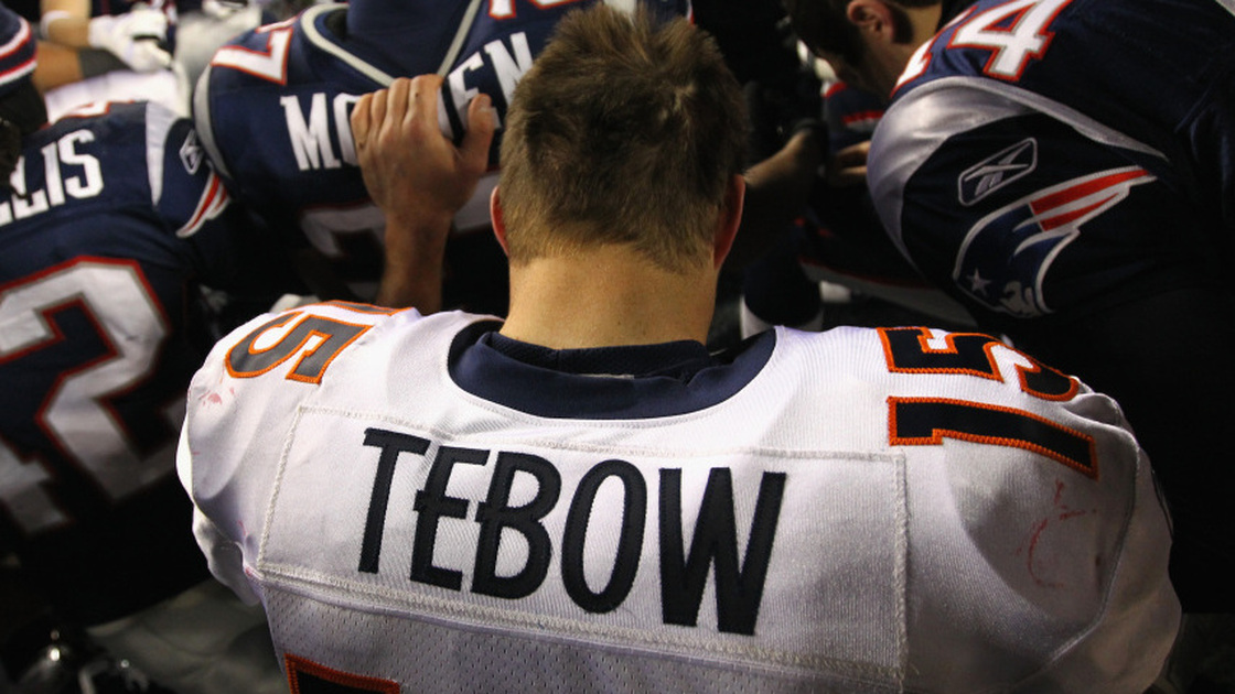 Tim Tebow of the Denver Broncos kneels and prays with teammates and members of the New England Patriots after the Patriots won 45-10 during their AFC Divisional Playoff Game at Gillette Stadium on January 14, 2012.