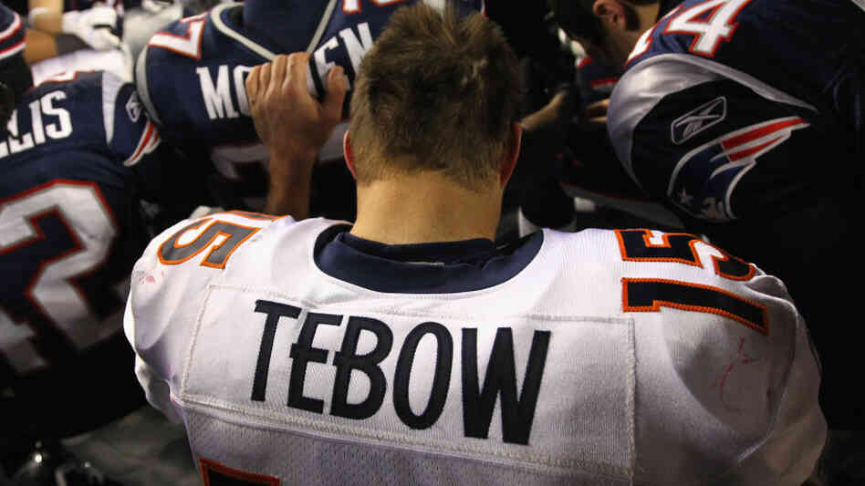 Tim Tebow of the Denver Broncos kneels and prays with teammates and members of the New England Patriots after the Patriots won 45-10 during their AFC Divisional Playoff Game at Gillette Stadium on January 14, 2012.