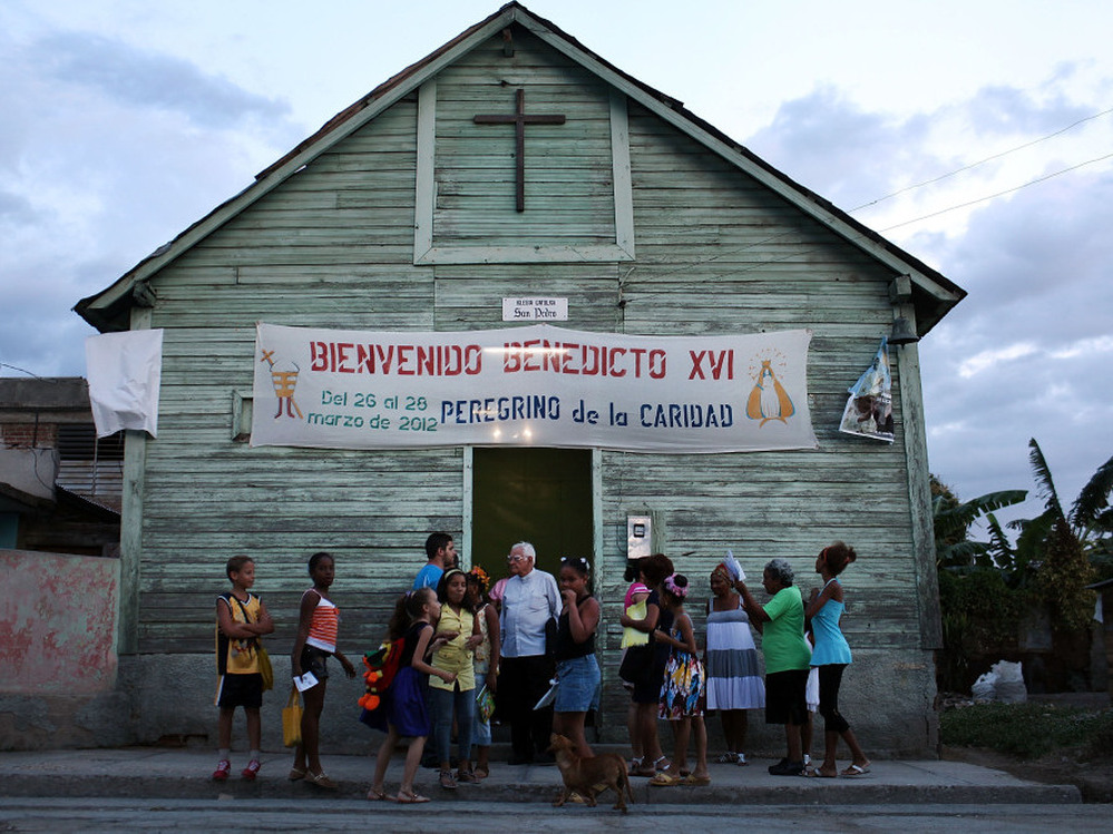 Parishioners stand outside a Catholic church in a poor Santiago suburb on Saturday in Cuba. Pope Benedict XVI is in Mexico but will head to Cuba next for a three-day visit.