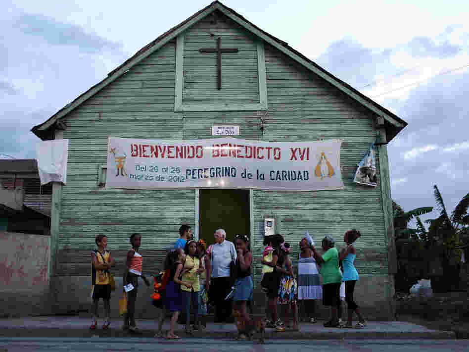 Parishioners stand outside a Catholic church in a poor Santiago suburb on Saturday in Cuba. Pope Benedict XVI is in Mexico but will head to Cuba next for a three-day visit.