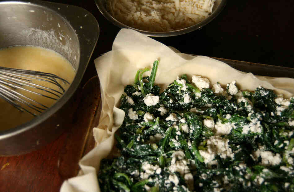 A pan is filled with alternating layers of spinach filling, dough and a cheesy custard.
