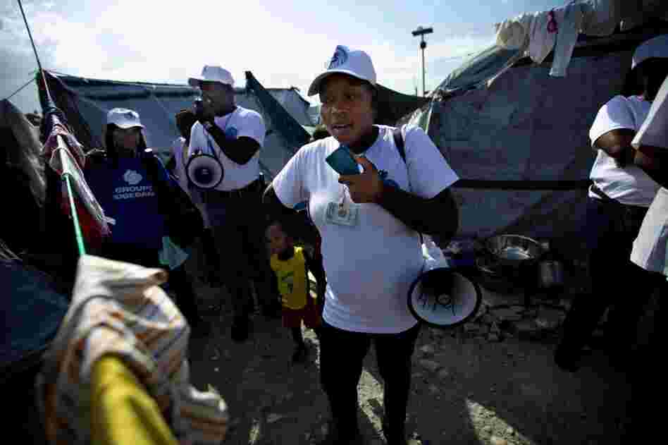 A GHESKIO worker walks through a tent camp in Port-au-Prince with a megaphone, warning people about the danger of cholera and the need for sanitation and clean water.