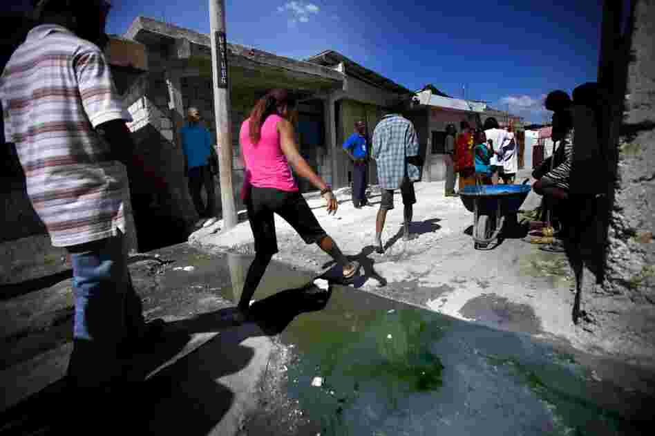 Residents of the Port-au-Prince slum Cite de Dieu step gingerly over a stream of sewage. Aid workers had planned to be finished with the vaccination program before the spring rains, when widespread flooding can bring cholera directly into people's homes.