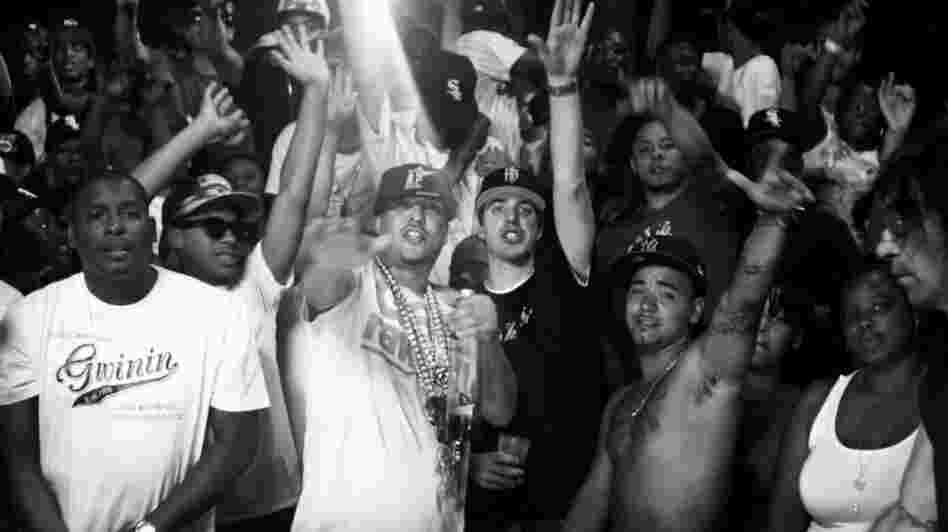 French Montana (in white shirt, chains and hat) and Harry Fraud (black shirt, black hat) at the center of the video for Montana's song "Shot Caller," which Fraud produced.