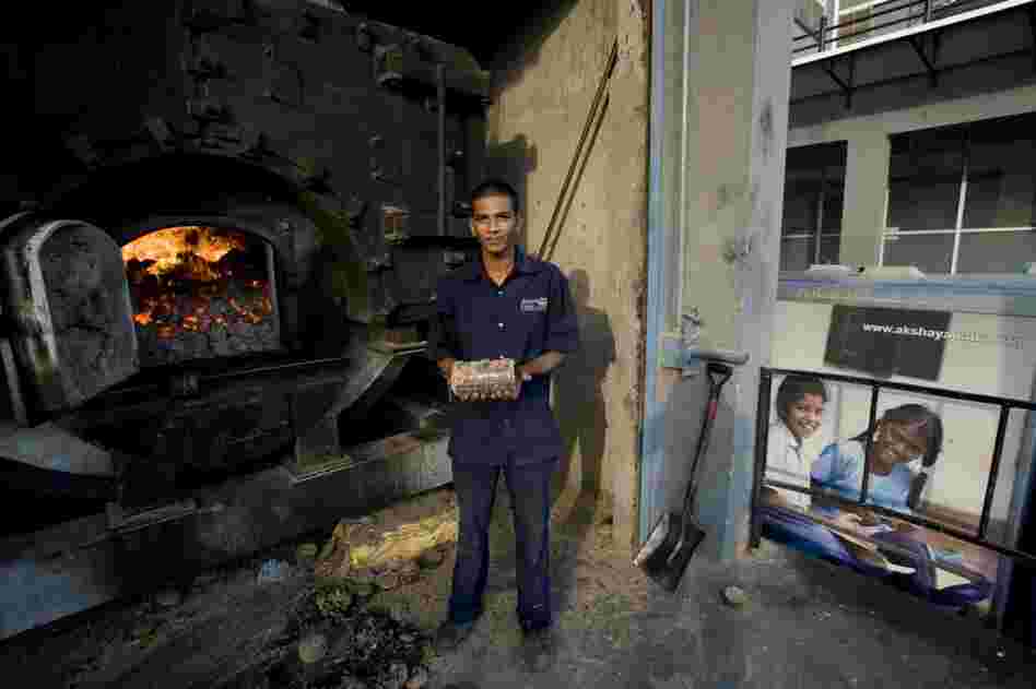 A workman holds a fuel briquette made from sugarcane waste, seed waste and peanuts. The briquette powers the kitchen's boilers.