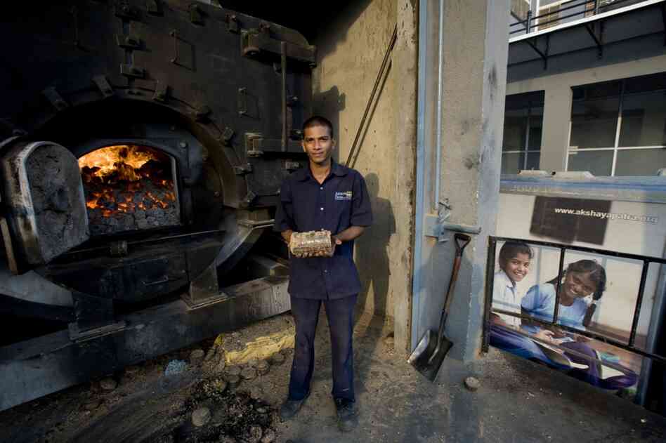 A workman holds a fuel briquette made from sugarcane waste, seed waste and peanuts. The briquette powers the kitchen's boilers.