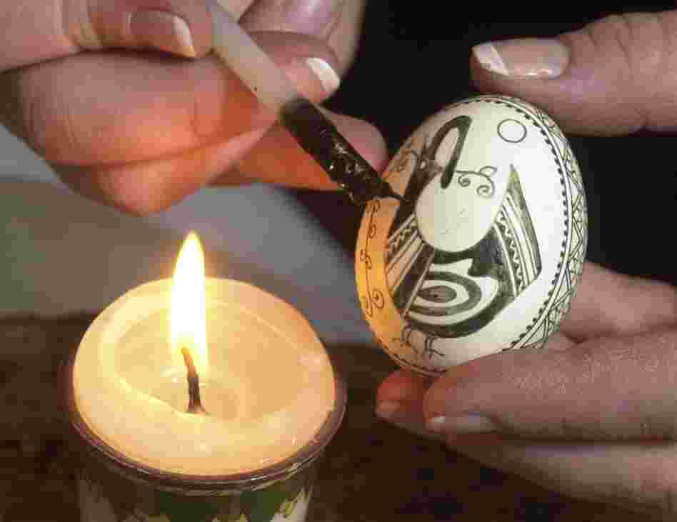 An artist uses a stylus to decorate an egg with melted wax, the traditional Ukrainian technique for crafting pysanka.