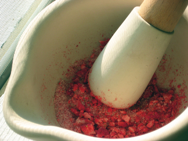 Sugar and dehydrated fruit are pulverized using a mortar and pestle.