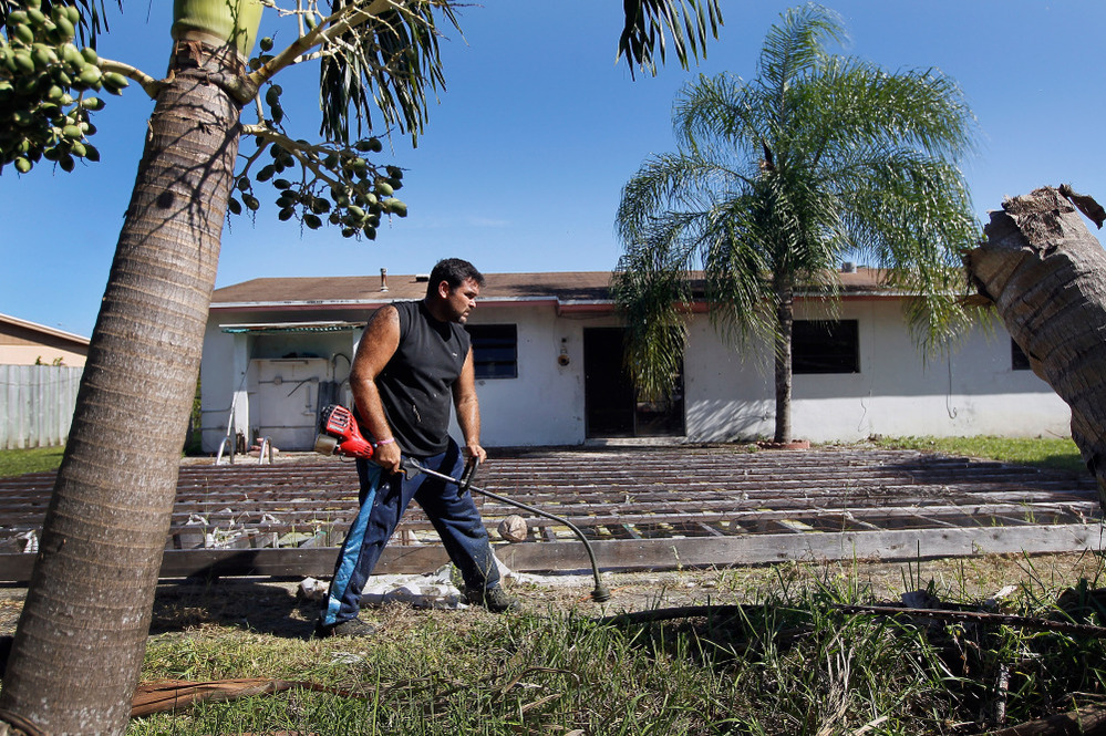 Renzo Salazar maintains the yard around a foreclosed house in Miami after the bank hired him to keep the home from falling into complete dilapidation. 