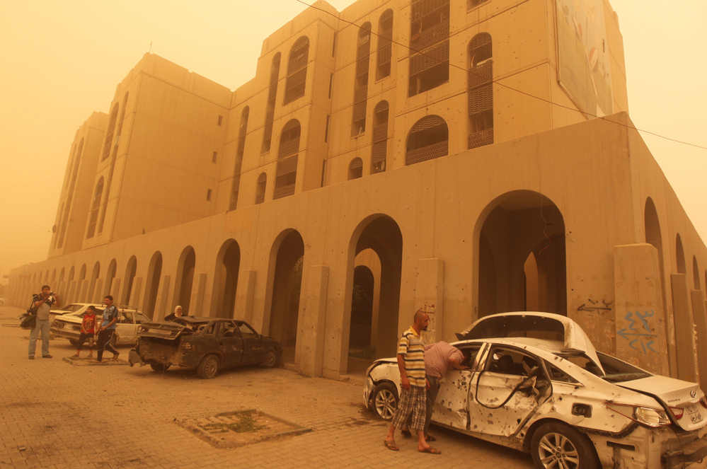 Iraqis inspect a car destroyed in a car bombing in Baghdad's Haifa Street, as dust creates a yellow haze across the city on Thursday.