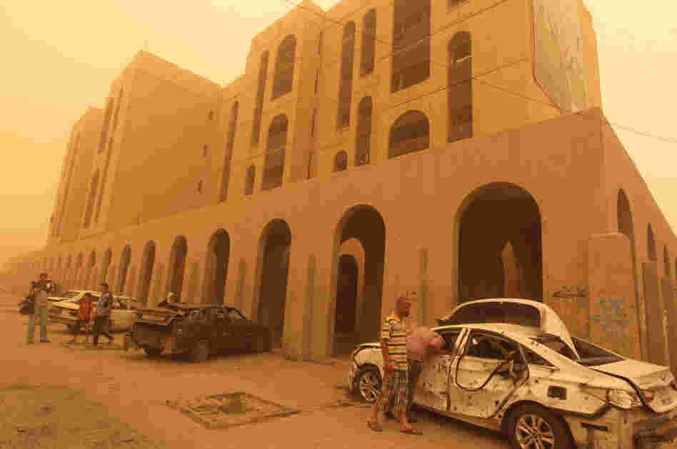 Iraqis inspect a car destroyed in a car bombing in Baghdad's Haifa Street, as dust creates a yellow haze across the city on Thursday.