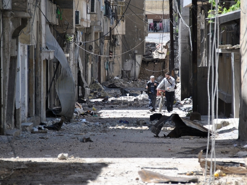 Syrians walk in an alley damaged by Syrian army shelling in the Bab Sbaa neighborhood in Homs province, central Syria, on April 21.