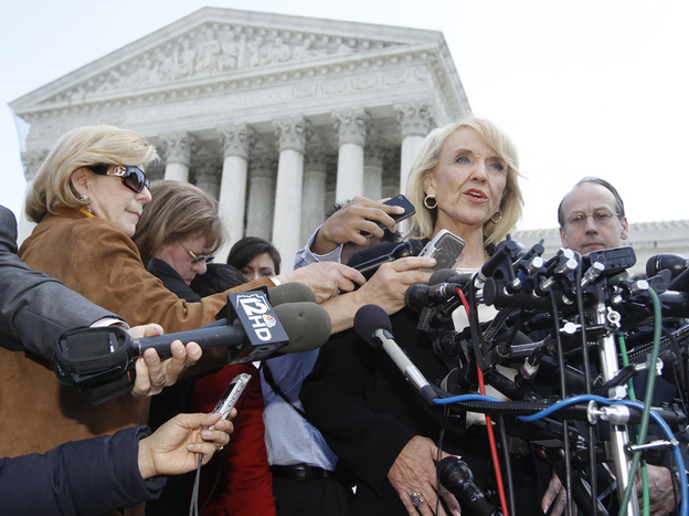Arizona Gov. Jan Brewer speaks to reporters outside the Supreme Court on Wednesday, after oral arguments on Arizona's immigration law. At left, in brown and wearing sunglasses, is NPR's Nina Totenberg.