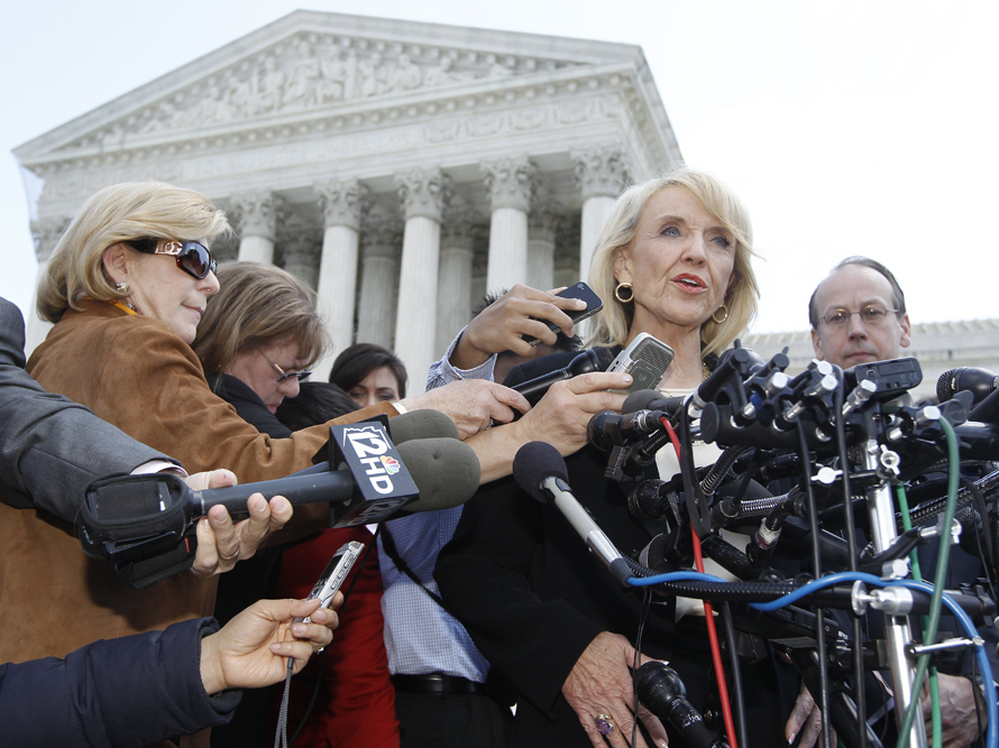 Arizona Gov. Jan Brewer speaks to reporters outside the Supreme Court on Wednesday, after oral arguments on Arizona's immigration law. At left, in brown and wearing sunglasses, is NPR's Nina Totenberg.