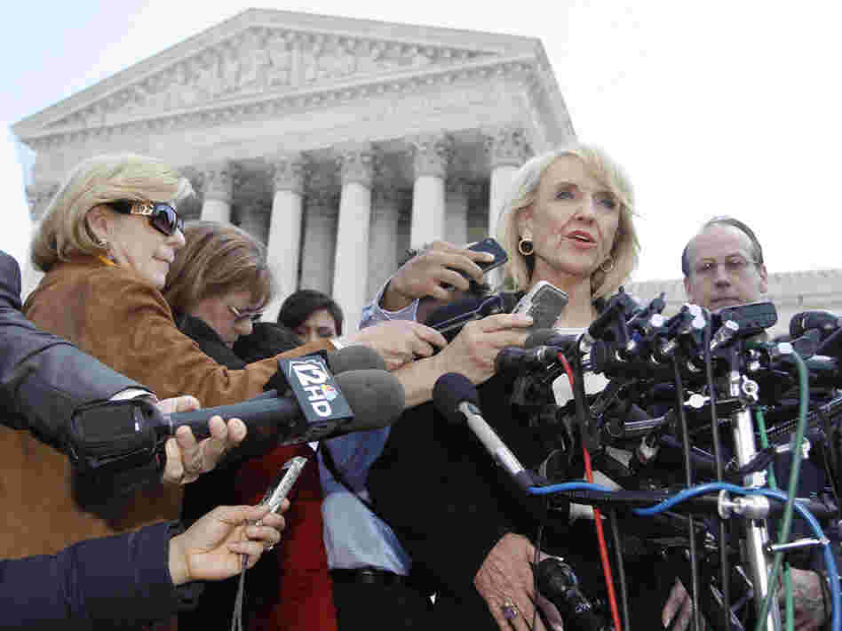 Arizona Gov. Jan Brewer speaks to reporters outside the Supreme Court on Wednesday, after oral arguments on Arizona's immigration law. At left, in brown and wearing sunglasses, is NPR's Nina Totenberg.