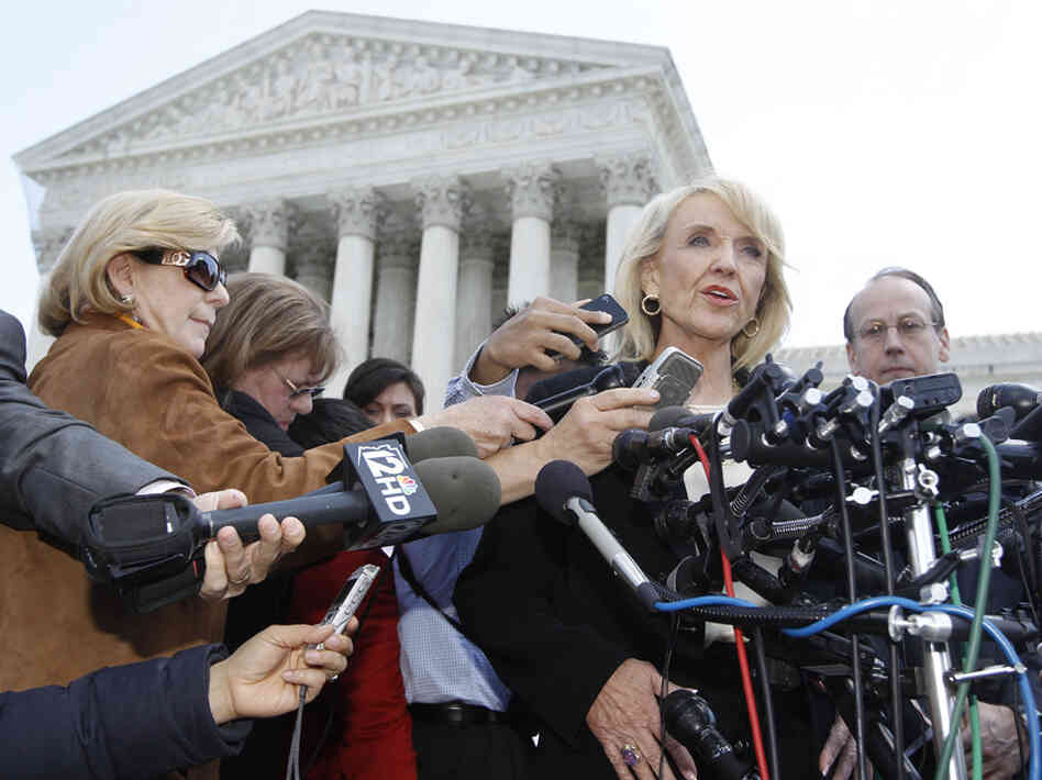 Arizona Gov. Jan Brewer speaks to reporters outside the Supreme Court on Wednesday, after oral arguments on Arizona's immigration law. At left, in brown and wearing sunglasses, is NPR's Nina Totenberg.