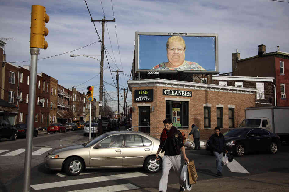 Pedestrians in Philadelphia cross a street in view of a billboard with a photo by Zoe Strauss. Only a dozen years after first picking up a camera to chronicle her beloved hometown's overlooked people and places, Strauss was honored with a solo show at the Philadelphia Museum of Art.