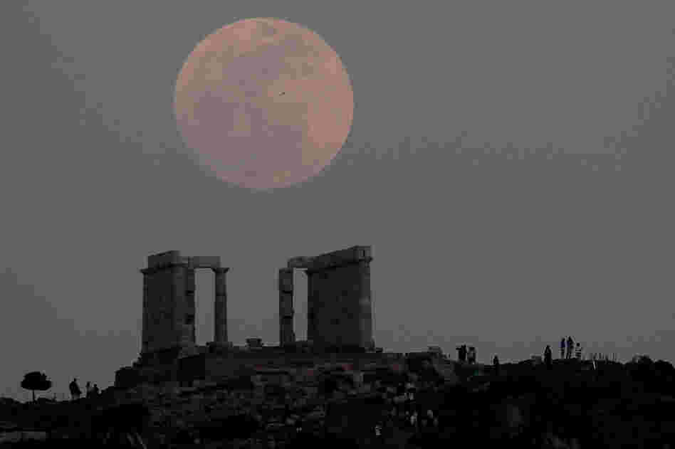 Tourists look at the moon rising over the ancient temple of Poseidon at cape Sounion, south of Athens. 