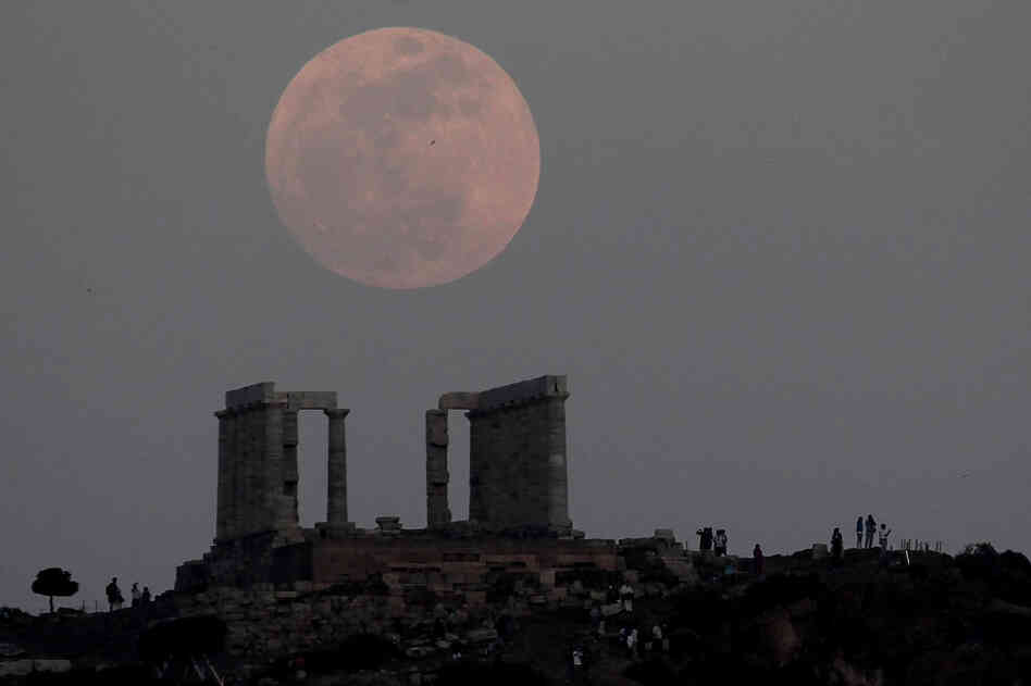 Tourists look at the moon rising over the ancient temple of Poseidon at cape Sounion, south of Athens. 