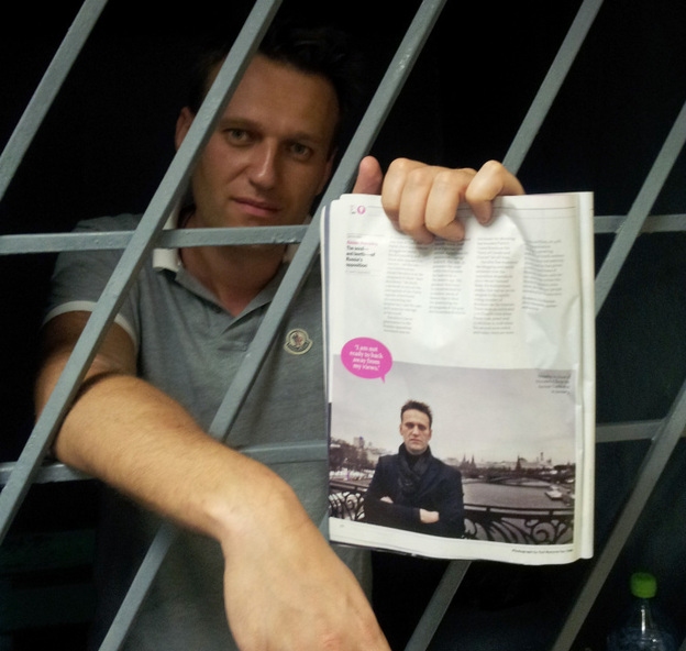 Alexei Navalny, a prominent anti-corruption whistleblower and blogger, holds an issue of Time Magazine, with his photograph, as he stands behind bars in a prison after he was detained in Moscow on Sunday.