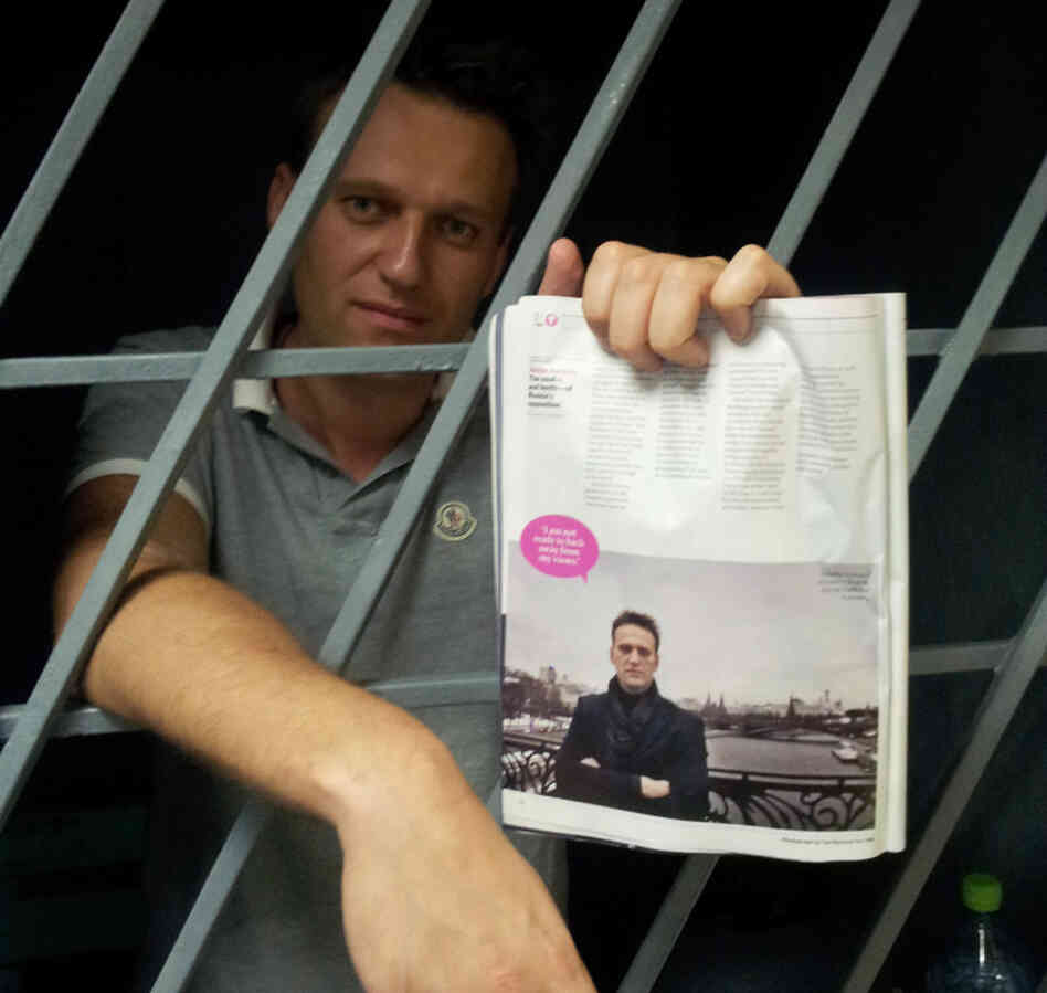 Alexei Navalny, a prominent anti-corruption whistleblower and blogger, holds an issue of Time Magazine, with his photograph, as he stands behind bars in a prison after he was detained in Moscow on Sunday.
