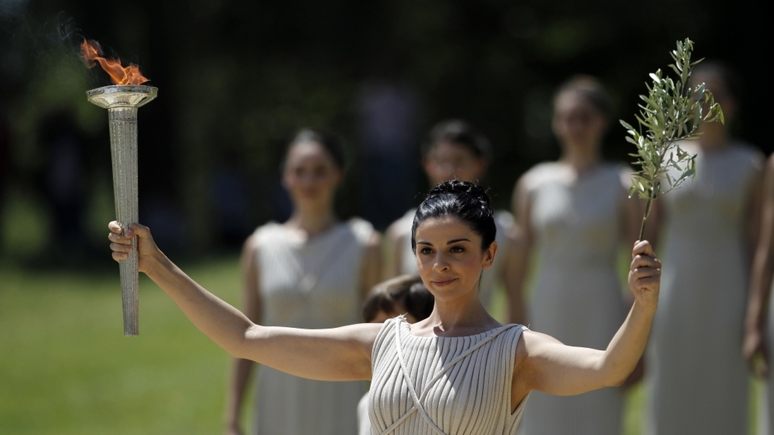 A priestess holds an olive branch and the lit Olympic torch.
