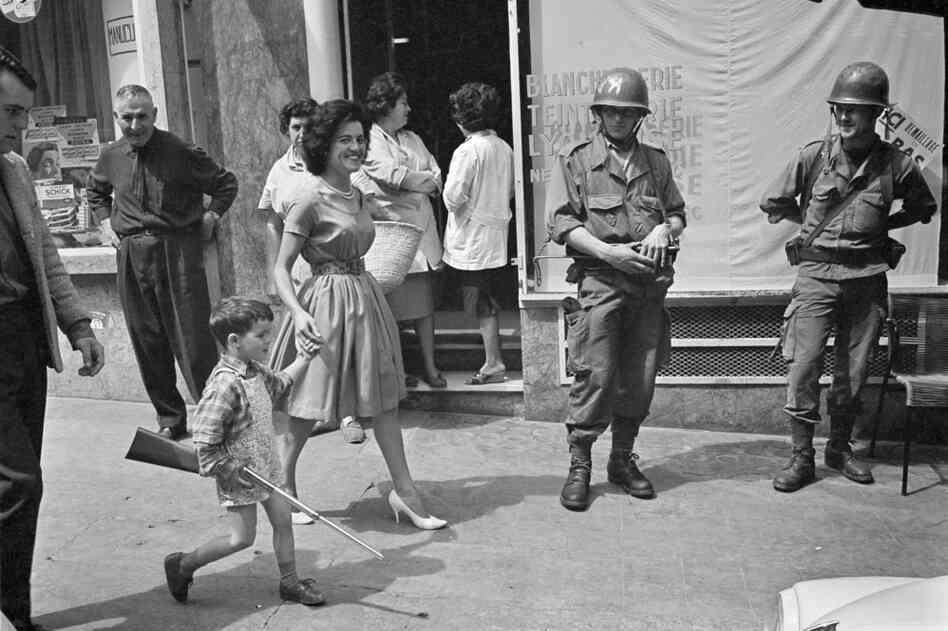 A boy carries a toy rifle past French soldiers at the Bastille Palace in Oran, Algeria, May 1962.