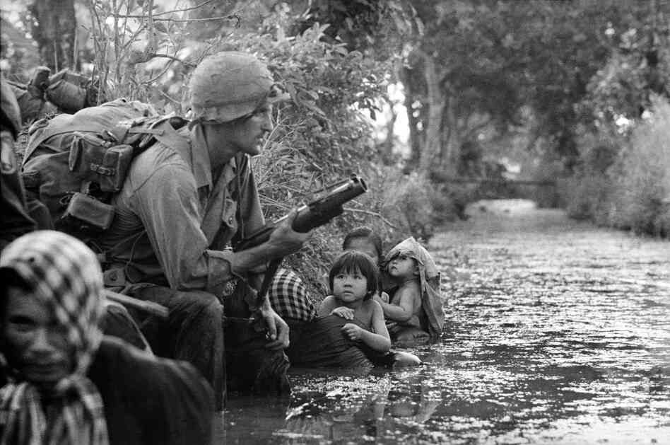South Vietnamese children gaze at an American paratrooper as they cling to their mothers, hiding from Viet Cong sniper fire west of Saigon, January 1966.