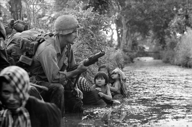 South Vietnamese children gaze at an American paratrooper as they cling to their mothers, hiding from Viet Cong sniper fire west of Saigon, January 1966.