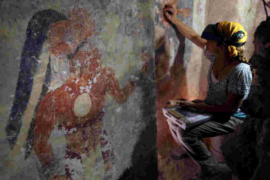 Conservator Angelyn Bass cleans and stabilizes the surface of a wall of a Mayan house that dates to the ninth century. The figure of a man who may have been the town scribe appears on the wall to her left.