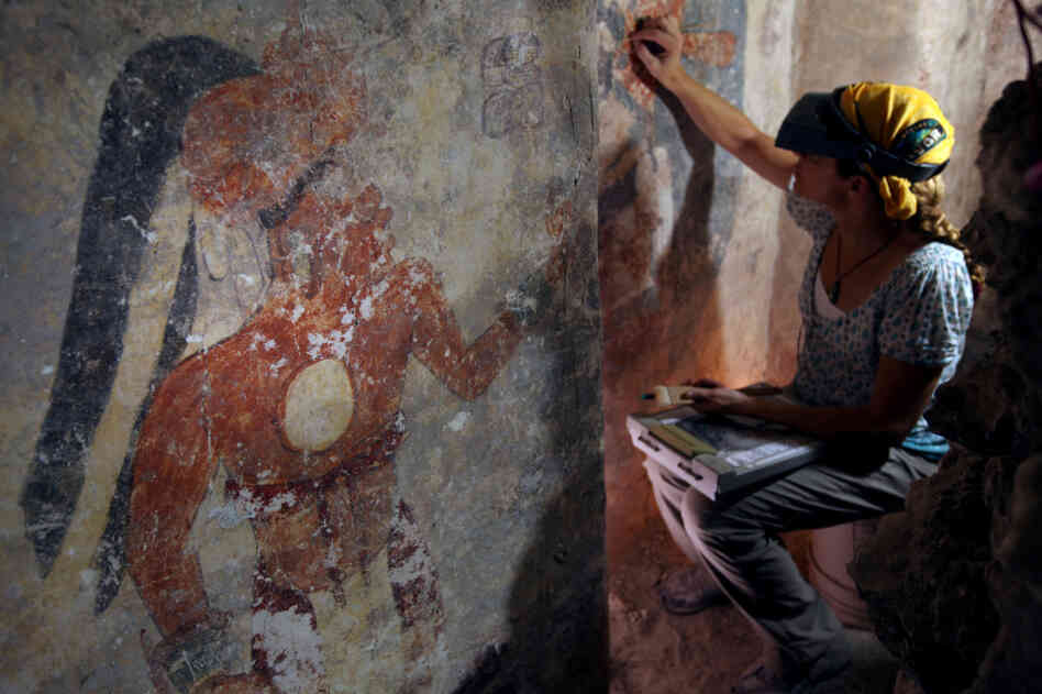 Conservator Angelyn Bass cleans and stabilizes the surface of a wall of a Mayan house that dates to the ninth century. The figure of a man who may have been the town scribe appears on the wall to her left.