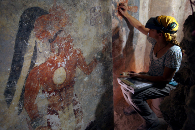 Conservator Angelyn Bass cleans and stabilizes the surface of a wall of a Mayan house that dates to the ninth century. The figure of a man who may have been the town scribe appears on the wall to her left. Conservator Angelyn Bass cleans and stabilizes the surface of a wall of a Mayan house that dates to the ninth century. The figure of a man who may have been the town scribe appears on the wall to her left.