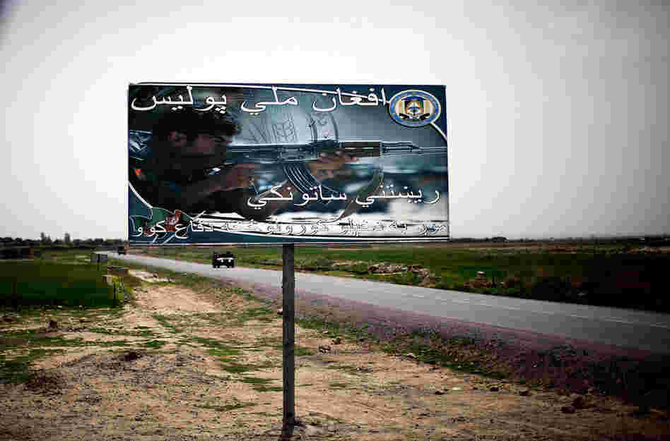 A billboard reads "Afghan National Police: The real guardian. We defend our own homes." It sits next to one of the main roads leading in and out of an area where the local population supports the Taliban.