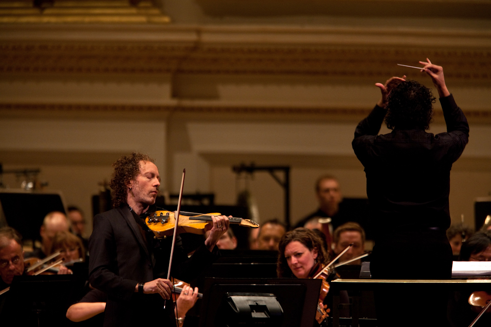 The concert also featured the New York premiere of Terry Riley's The Palmian Chord Ryddle for Electric Violin and Orchestra, a piece he wrote for the soloist, Tracy Silverman. Silverman designed his own six-string instrument that reaches down into the cello range. 