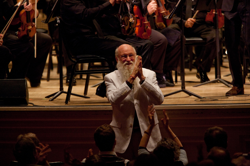 Terry Riley accepting enthusiastic applause. He said that his concerto "leaped into my consciousness as a very spontaneous work, full of the things in music that I find colorful, dynamic, beautiful, challenging, humorous, loving, friendly, joyous, stark and universally minded."