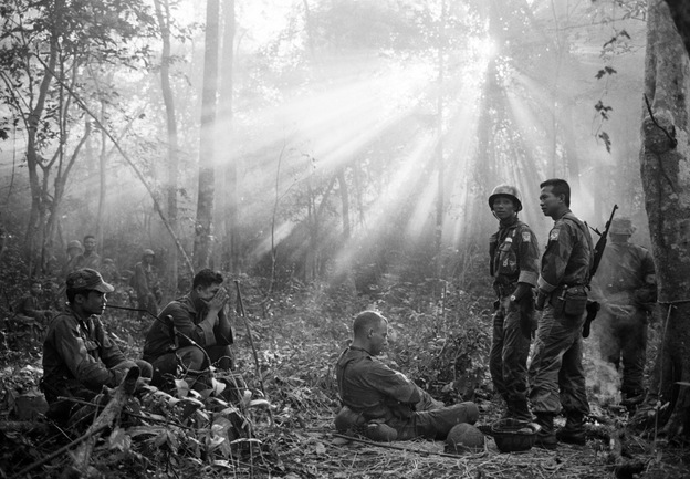 The sun breaks through dense jungle foliage as South Vietnamese troops, joined by U.S. advisers, rest after a cold, damp and tense night of waiting in an ambush position for a Viet Cong attack that didn't come, January 1965.