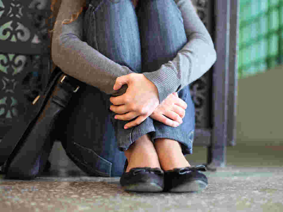 A teenage girl sits on the floor with her hands crossed over her legs. A teenage girl sits on the floor with her hands crossed over her legs.