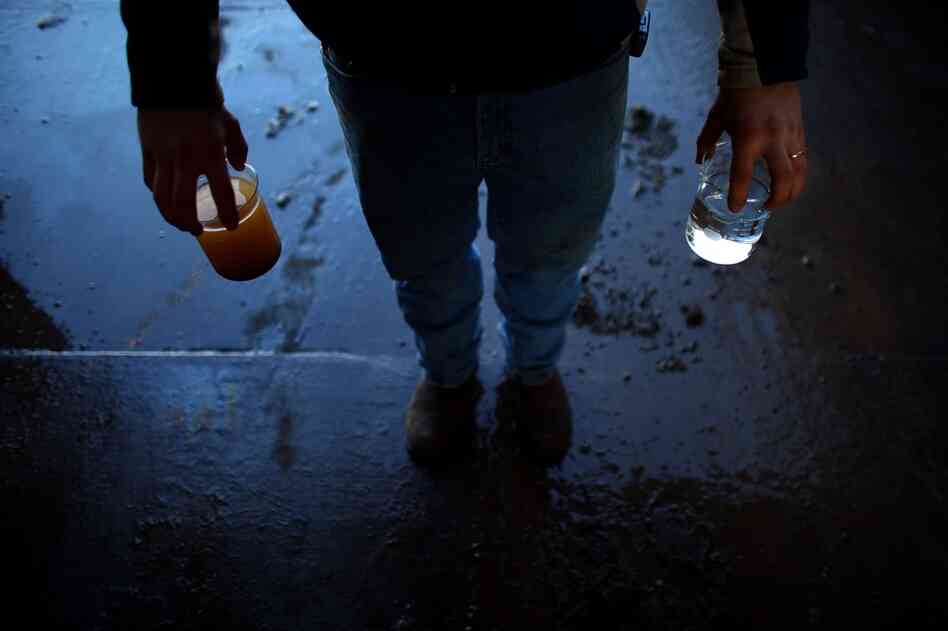 A worker at Eureka Resources, a recycling plant, holds a container of purified water (right) and wastewater from a gas well (left).