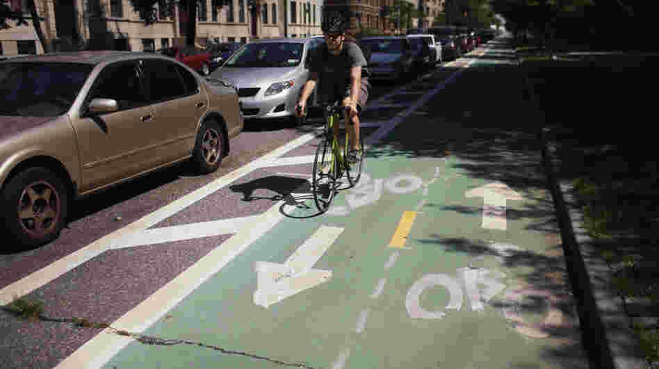A cyclist rides on a bike lane on Prospect Park West, in the Brooklyn borough of New York City. Bike lanes of this type use parked cars to create a buffer zone from road traffic.