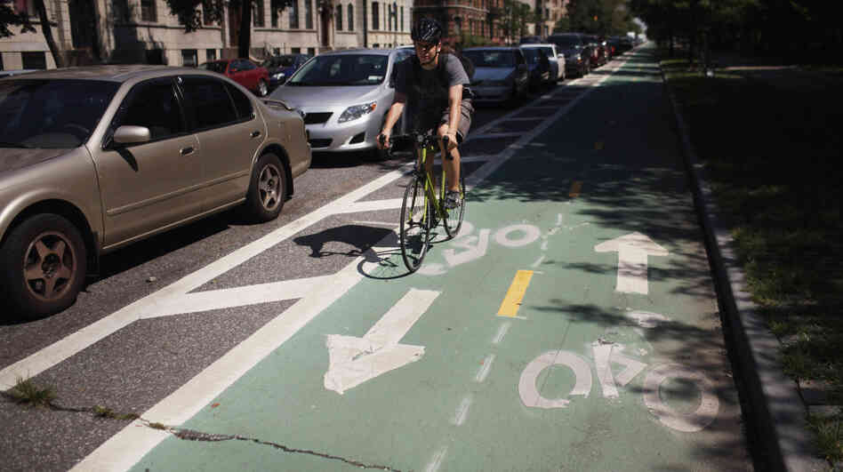 A cyclist rides on a bike lane on Prospect Park West, in the Brooklyn borough of New York City. Bike lanes of this type use parked cars to create a buffer zone from road traffic.