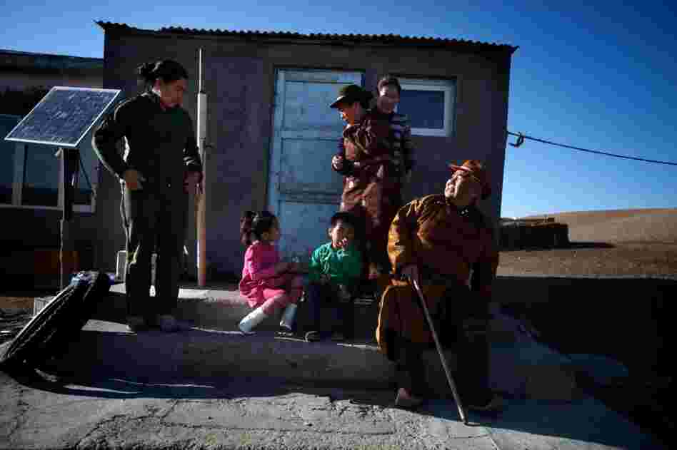 Mijiddorj Ayur (right) sits with his extended family outside his house in South Gobi. He wears traditional clothes, including boots with curled-up toes.