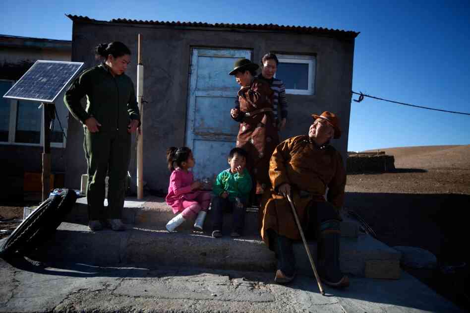 Mijiddorj Ayur (right) sits with his extended family outside his house in South Gobi. He wears traditional clothes, including boots with curled-up toes.