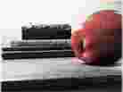 An apple rests on a desk next to a pile of books. An apple rests on a desk next to a pile of books.