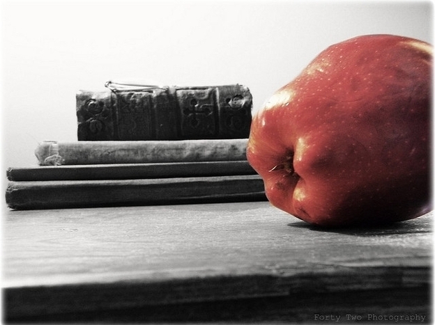 An apple rests on a desk next to a pile of books.