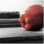 An apple rests on a desk next to a pile of books.