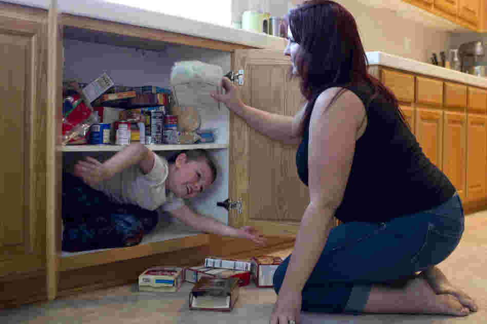 Jaden climbs into a kitchen cabinet, removing the food from the shelves so he can fit. Amber says she can't afford to buy him new shoes or clothes because of her health care expenses.