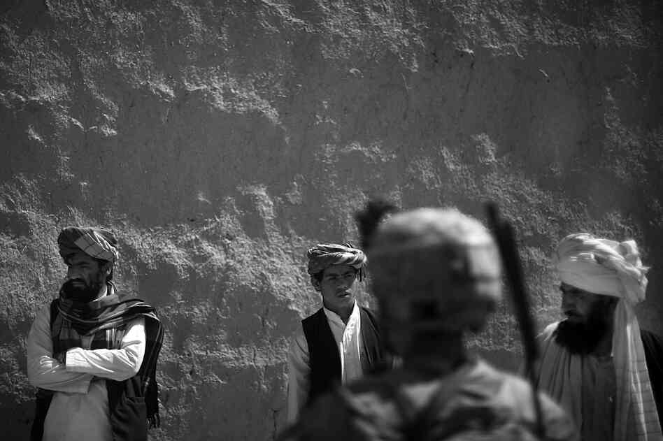 A soldier stands in front of a group of men from Babaker, while they wait to be questioned by Afghan National Army troops.